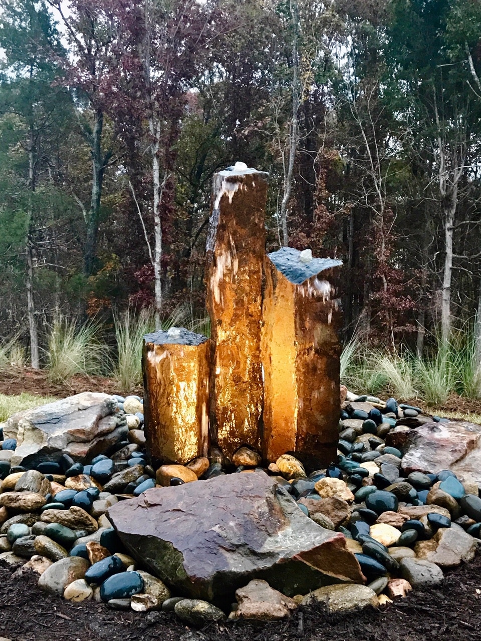 A large rock fountain in the middle of a wooded area.