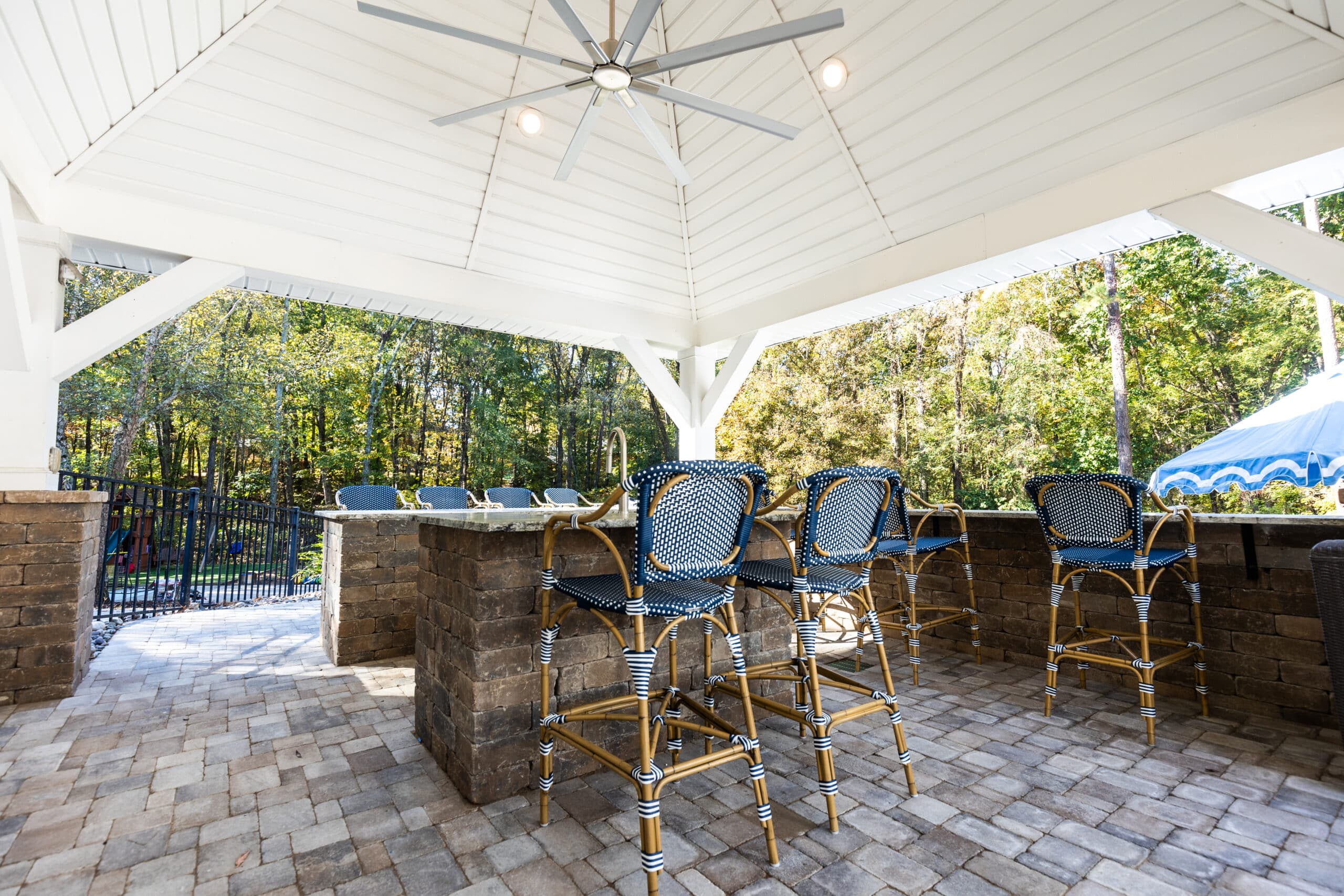 A brick patio with blue chairs and a ceiling fan.