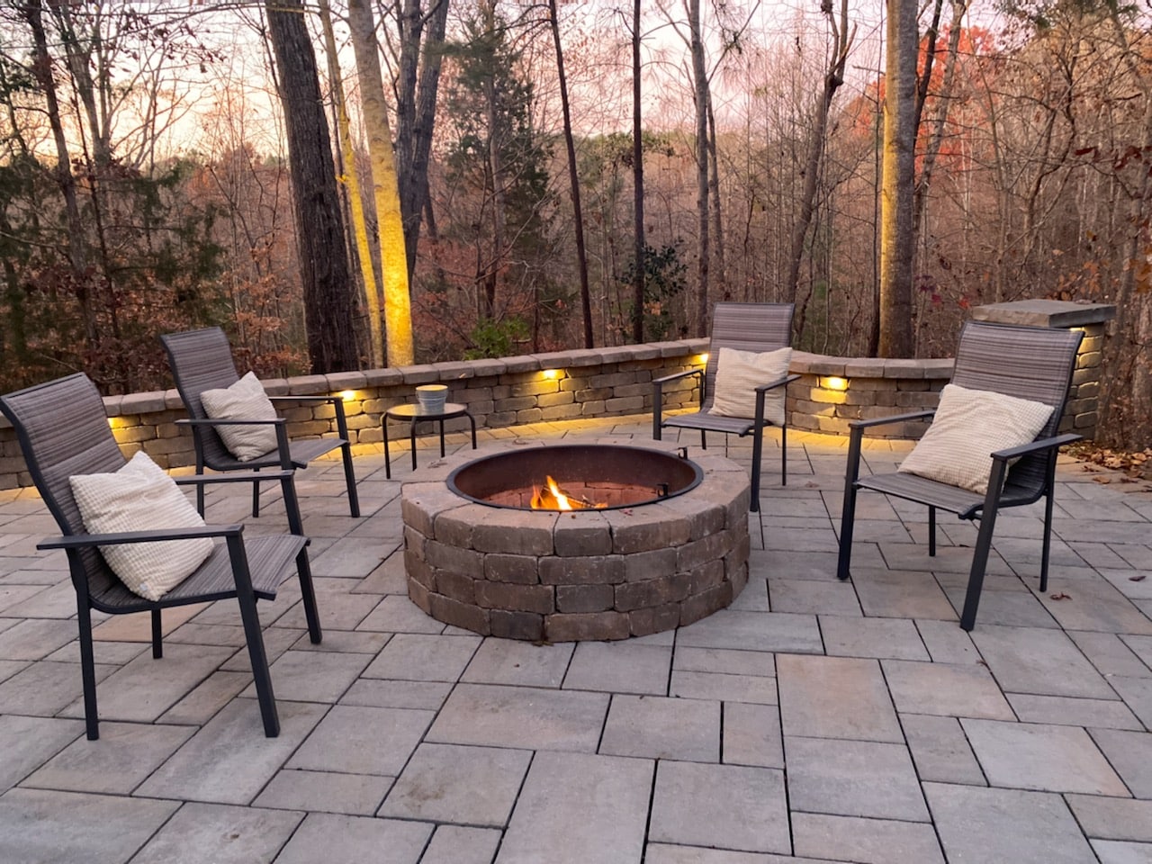 A patio with a fire pit in the middle of a wooded area.