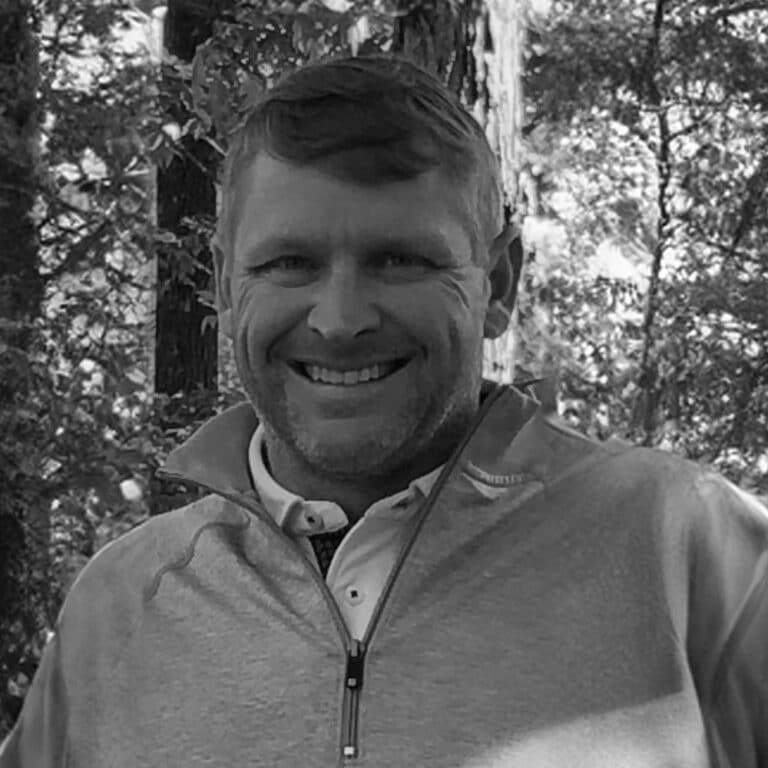 A black and white photo of a man smiling in the woods.