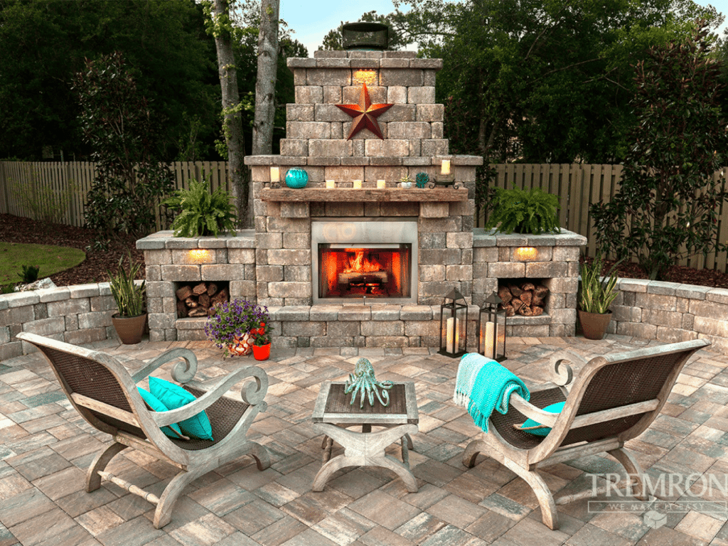 A beautiful hardscape design patio with a fire pit and chairs.