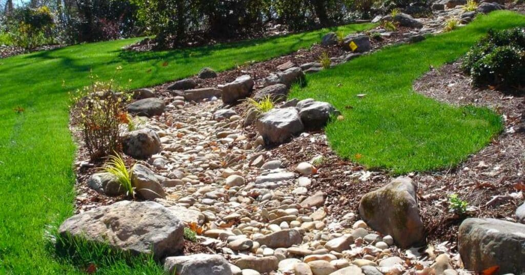 A stream in a garden with rocks and grass. 