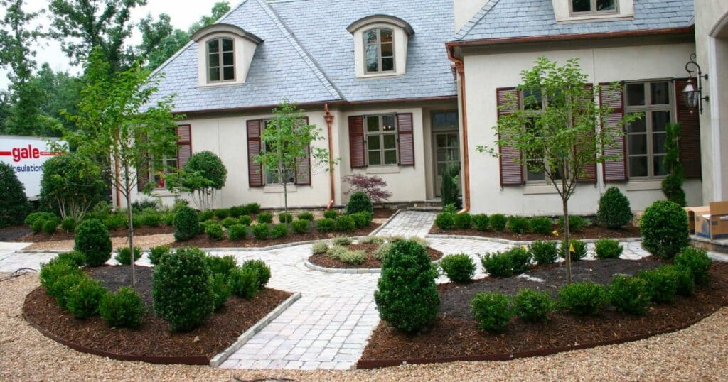 A front yard with bushes and shrubs in front of a house, designed by a landscape design company