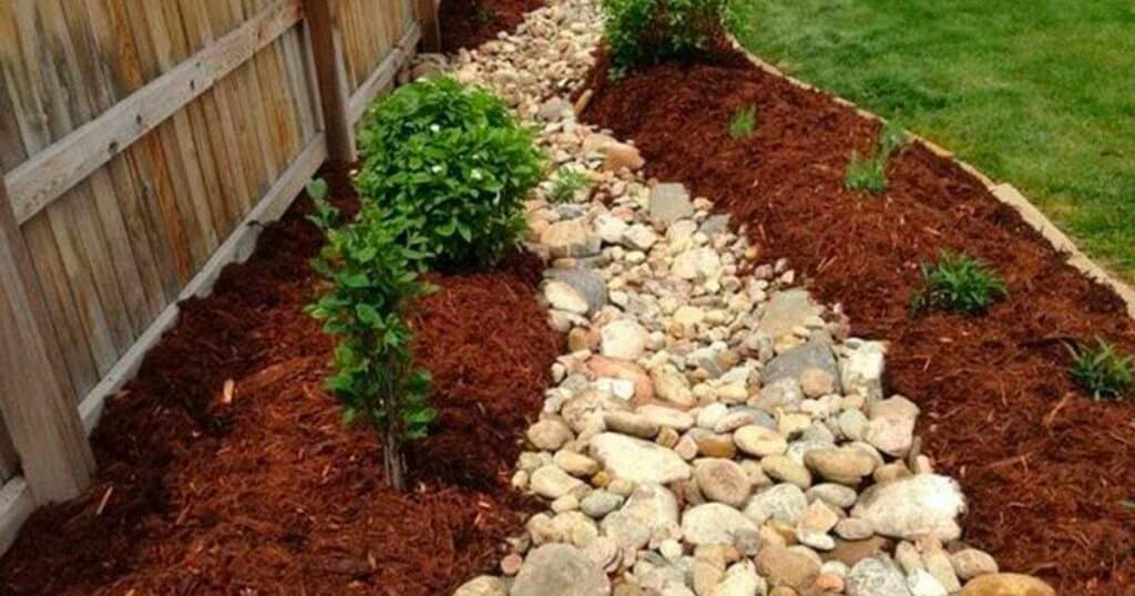 A small stream in a backyard with rocks and gravel.