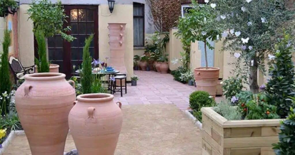 An inviting courtyard featuring large terracotta pots, flowering plants, and a cozy seating area.