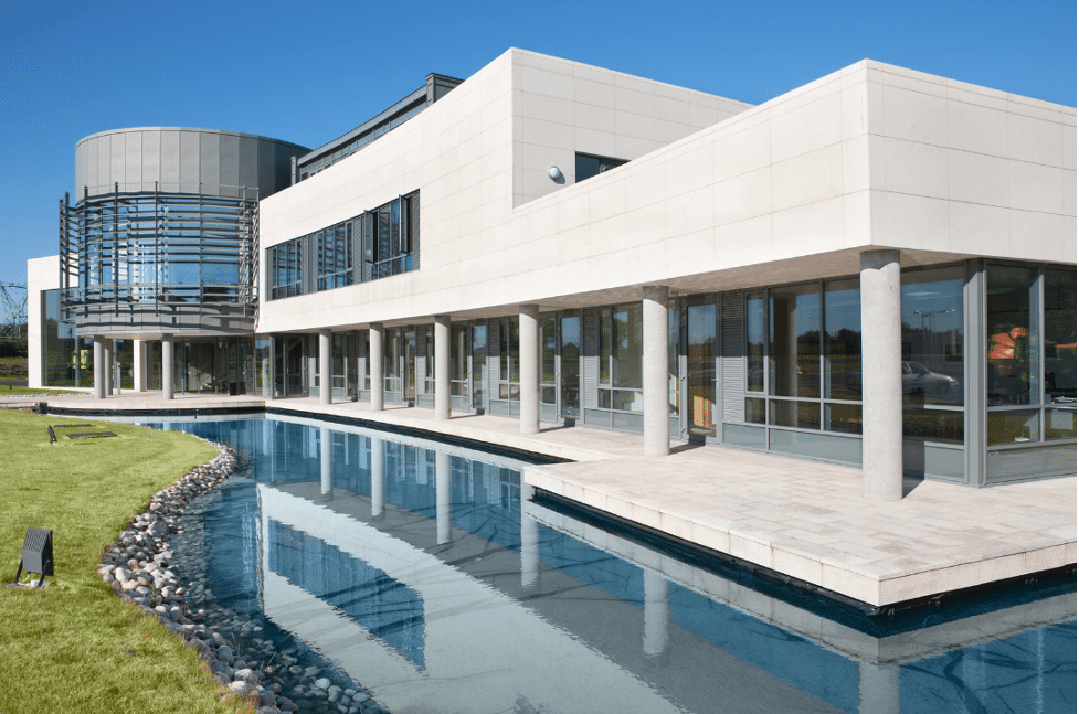 Modern building with a combination of glass and concrete architecture, featuring a reflecting pool and green lawn in front, under a clear blue sky.