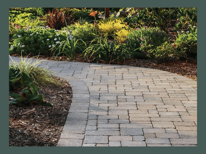 A curved stone pathway surrounded by various green plants, flowers, and mulch in a garden setting.