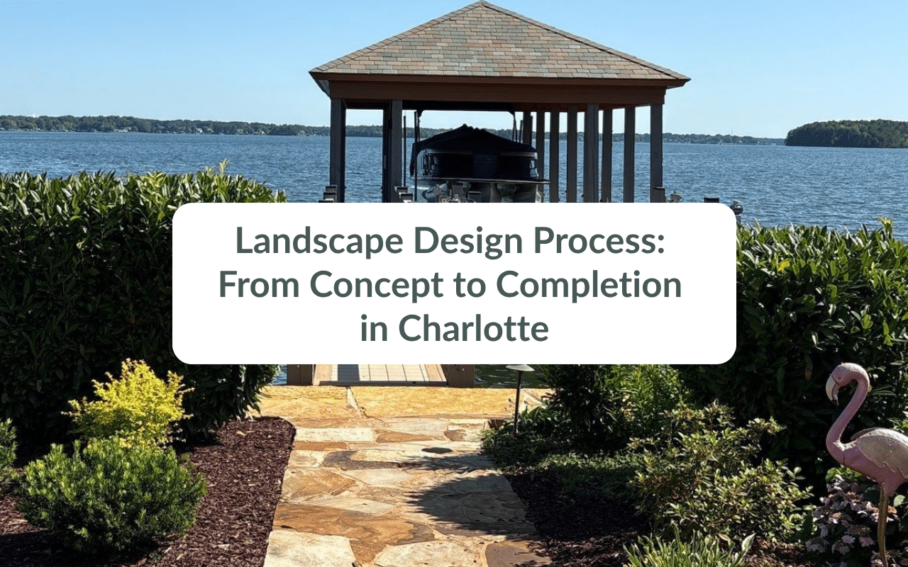 A landscaped garden path leads to a covered dock on a lake, with shrubs, mulch, and a pink flamingo ornament visible in the foreground.